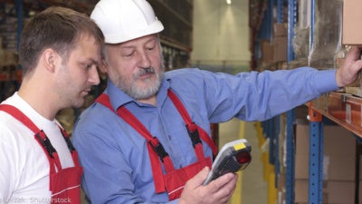 Older working training a younger worker in a warehouse