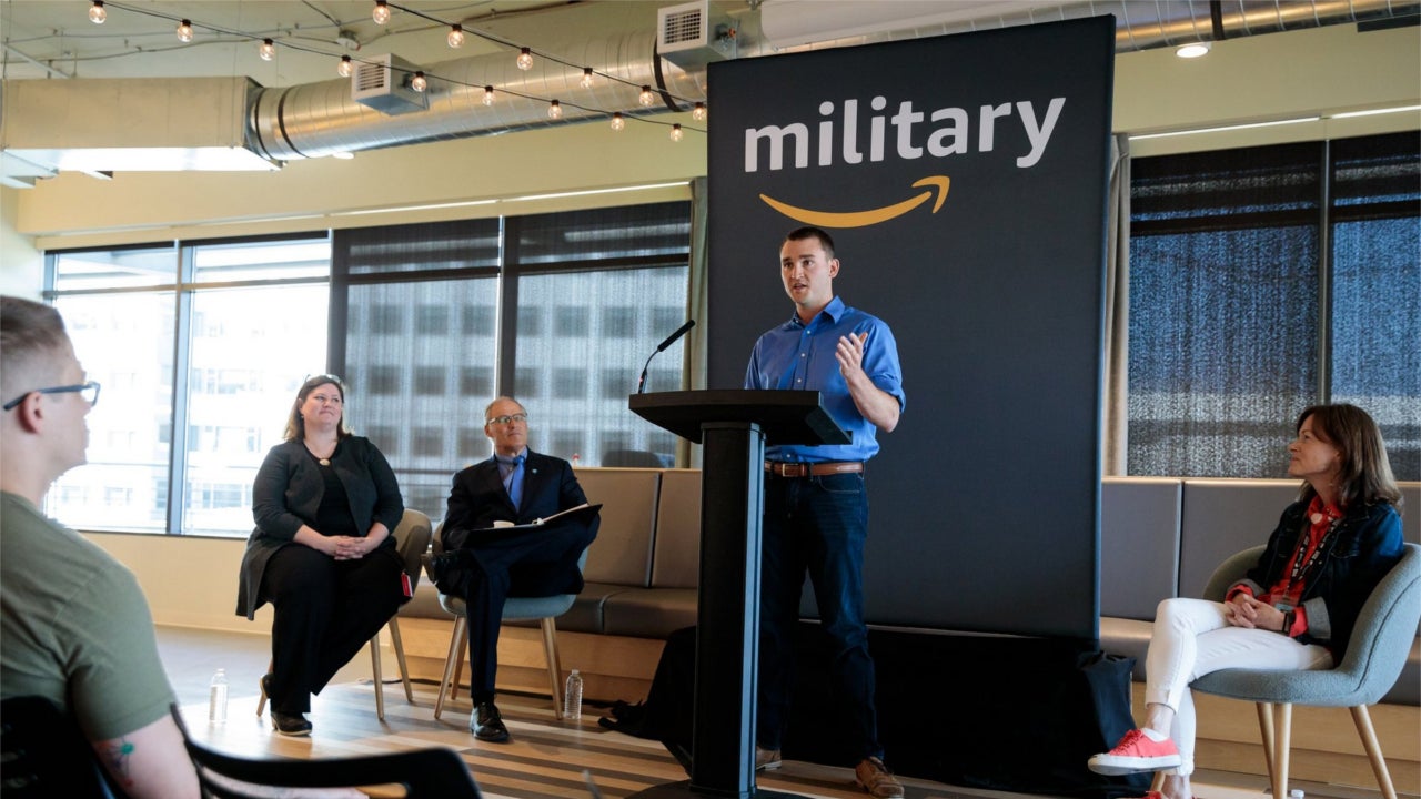 Mike Cooper, a Coast Guard veteran and new Amazon employee, at a ceremony for graduates of an apprenticeship program that trains military veterans for technology jobs at Amazon. Seated are Jennifer Carlson, of the Washington Technology Industry Association, Washington Gov. Jay Inslee and Ardine Williams, an Amazon vice president. (Jordan Stead / Amazon)