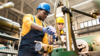 Photo of two manufacturing workers in protective gear operating a lathe
