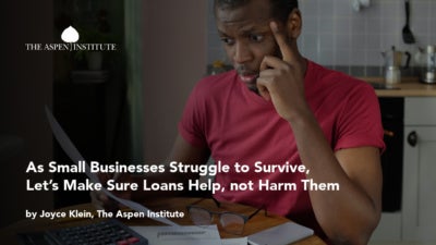 Foreground: "As Small Businesses Struggle to Survive, Let’s Make Sure Loans Help, not Harm Them by Joyce Klein, The Aspen Institute." Background: Photo of a concerned Black business owner staring at financial documents in front of a laptop, with glasses and calculator nearby.