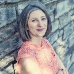 Elizabeth has chin-length black and gray hair and is standing in front of a stone wall.