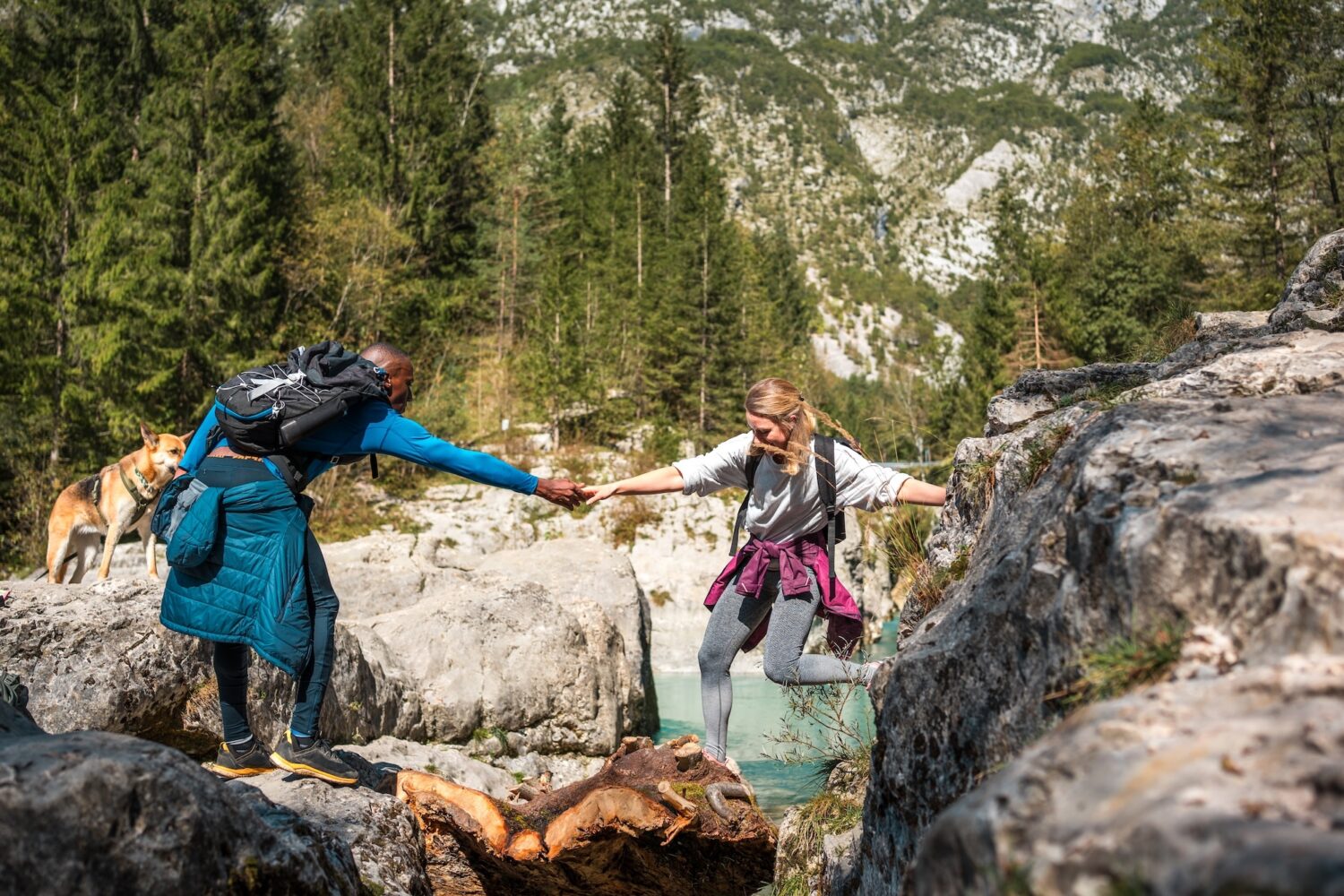A person in hiking gear helps another person in hiking gear cross a river, representing trust-building in tech.