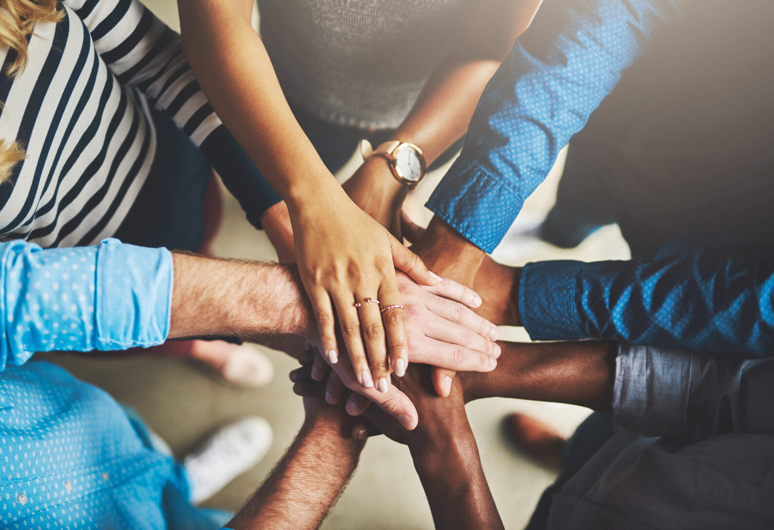 A close-up photo of hands overlapping in a circle. It represents the Alliance for Social Trust.