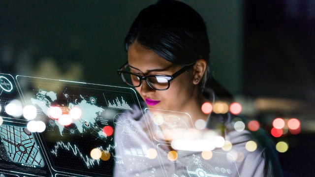 Photo of a Latin woman in glasses looking at charts on a futuristic screen.