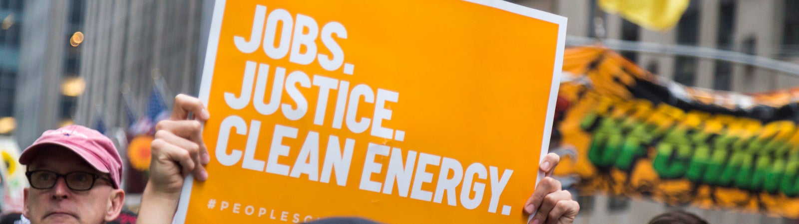 Photo of a person carrying a placard supporting "Jobs, Justice, Clean Energy".