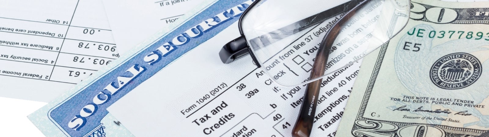 Photo of a Social Security card, 1040 form, $20 bill, and glasses on a table
