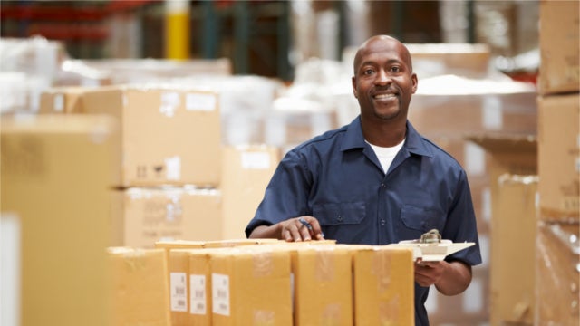 Smiling warehouse worker holding a clipboard near a stack of boxes
