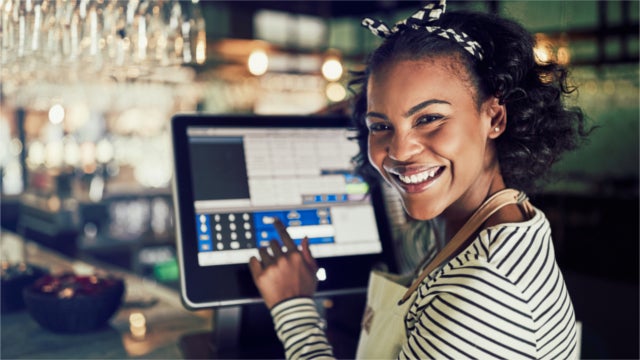 Photo of a smiling Black woman using a touchscreen cash register