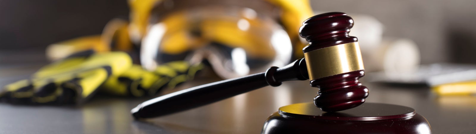 Photo of a gavel with a hard hat, safety googles, and work gloves in the background.