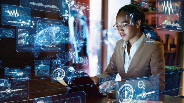 Photo of a woman working at a laptop with technology symbols floating around her