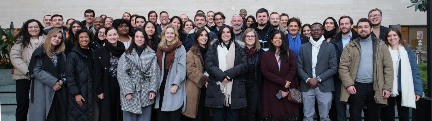 A large group of people, dressed in coats and business wear, stand on concrete steps smiling.