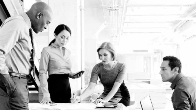 Group of workers in business attire talking around conference table.