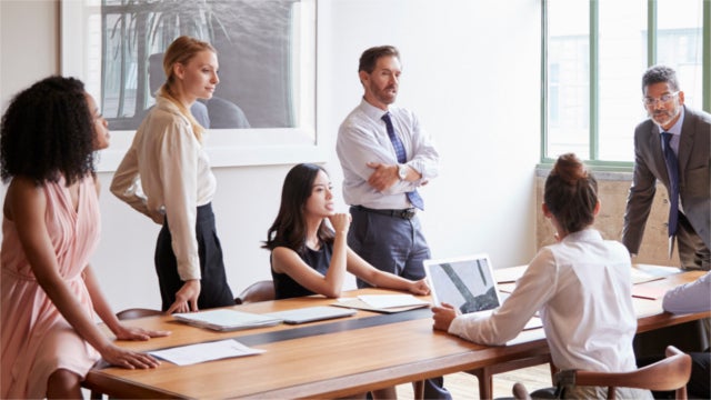 Group of workers in business attire talking around conference table.