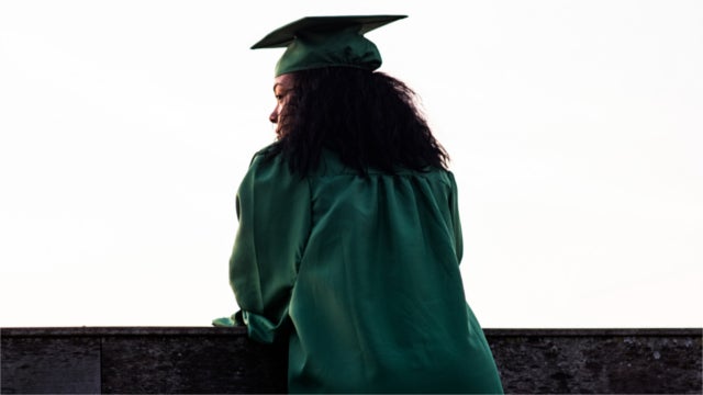 Woman in graduation cap and gown staring into the distance
