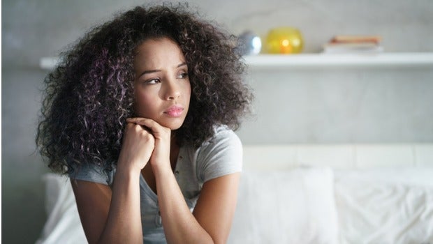 A woman sitting on her bed looking sad.
