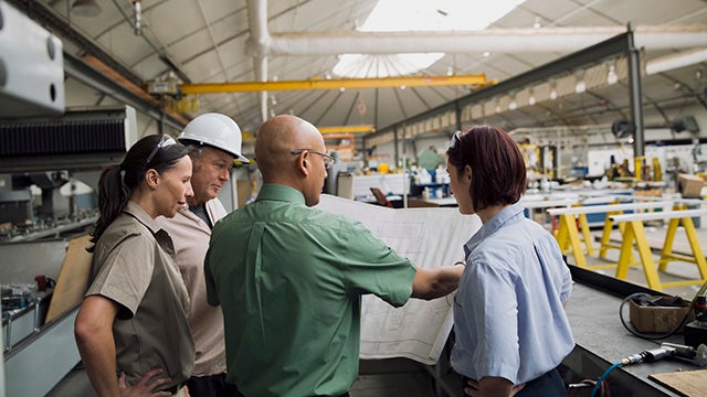 Workers reviewing blueprints in manufacturing plant
