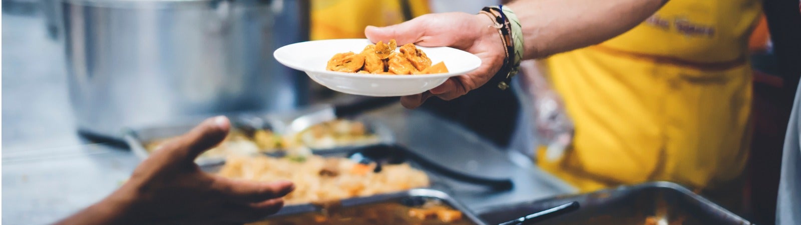 A volunteer hands a plate of food to someone in line at a soup kitchen.