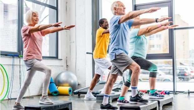 A group of seniors exercising on step platforms in a gym.