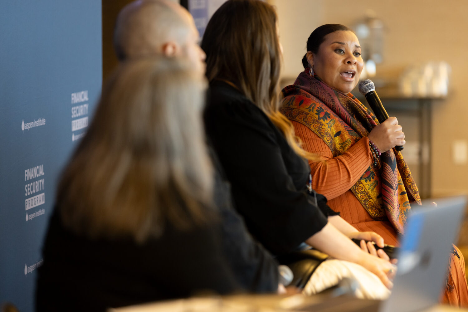 A woman holds a microphone while speaking on an event panel.